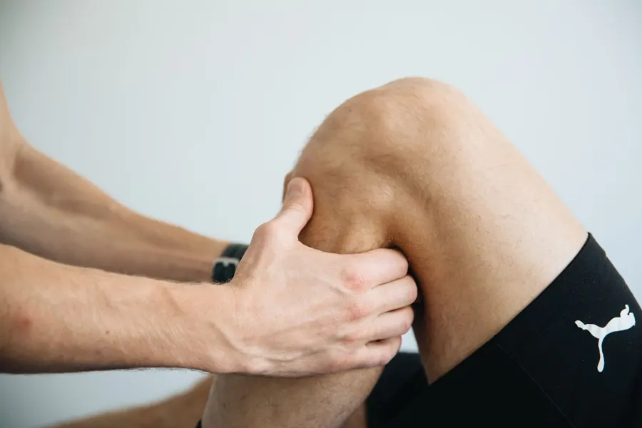 Handen van de therapeut rond een knie