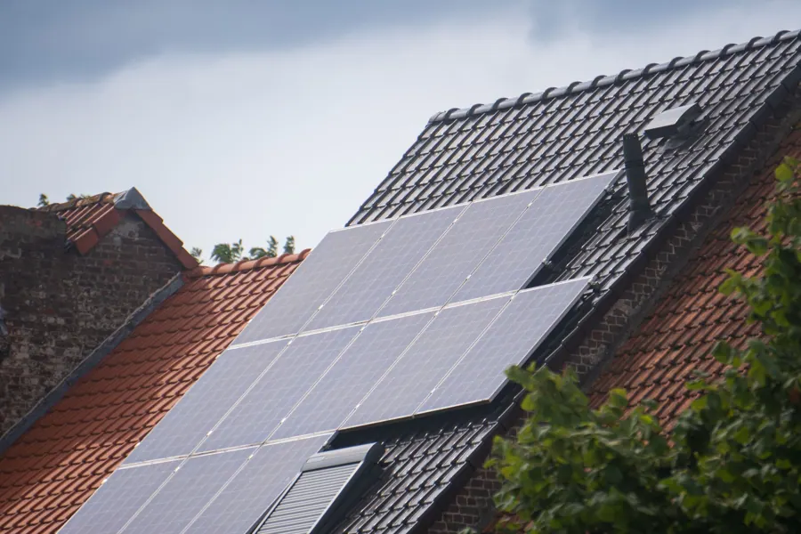 Zonnepanelen op een schuin dak met donkere pannen tussen de bomen