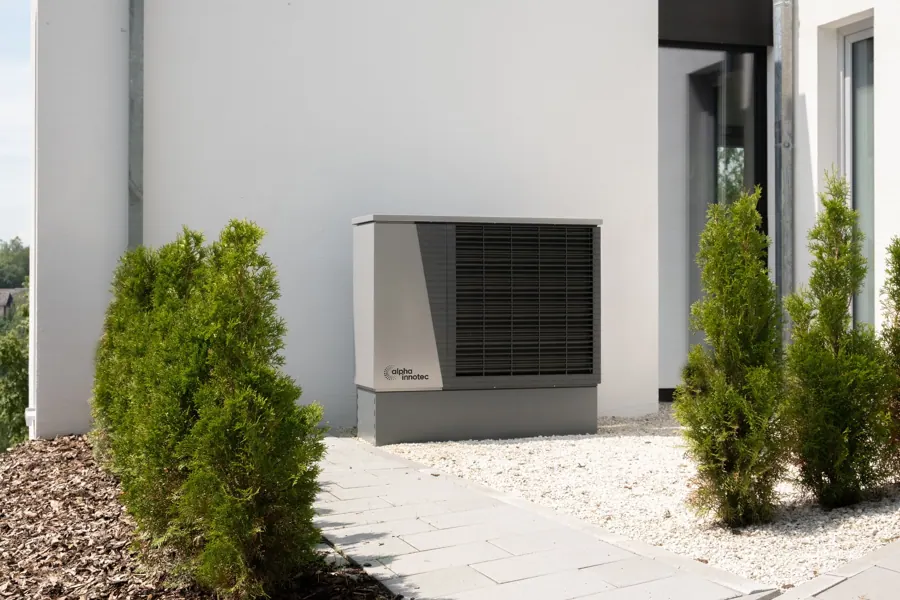 Buitenunit van een warmtepomp tegen een witte gevel