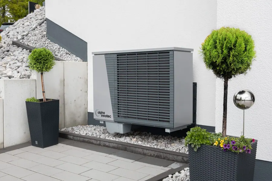 Warmtepomp op een grindbed tussen potten met buxus